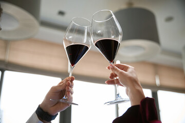 Close up of man and woman clinking glasses of red wine in the restaurant, holding up