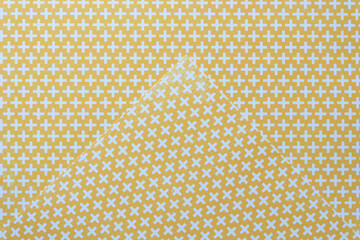 corner of scrapbooking sheet in yellow with repeating cross pattern on same 