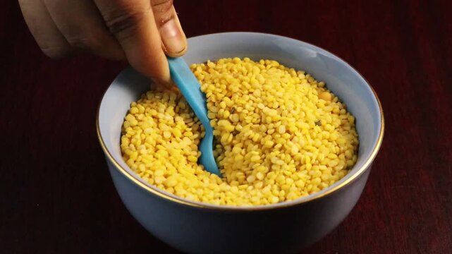 Spilt of yellow Moong bean (Vigna radiate) or Green Gram beans on bowl footage. A women taking moong dal by spoon. 