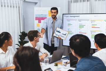 Project manager communicate and collaborate with team using project management software display on monitor, tracking progress of project task and making schedule plan at meeting table. Prudent