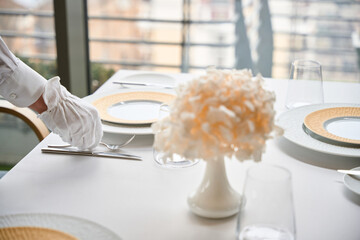 Hand of male waiter in white glove setting a table in luxury restaurant