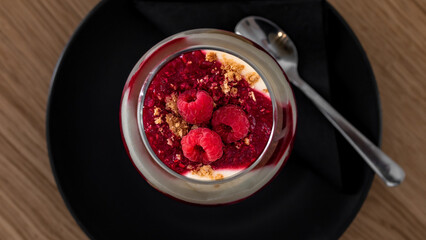 Raspberries and vanilla cream in a glass on a plate with a spoon.
