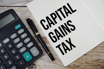 Capital gains tax text message written on note page with calculator top view on wooden background