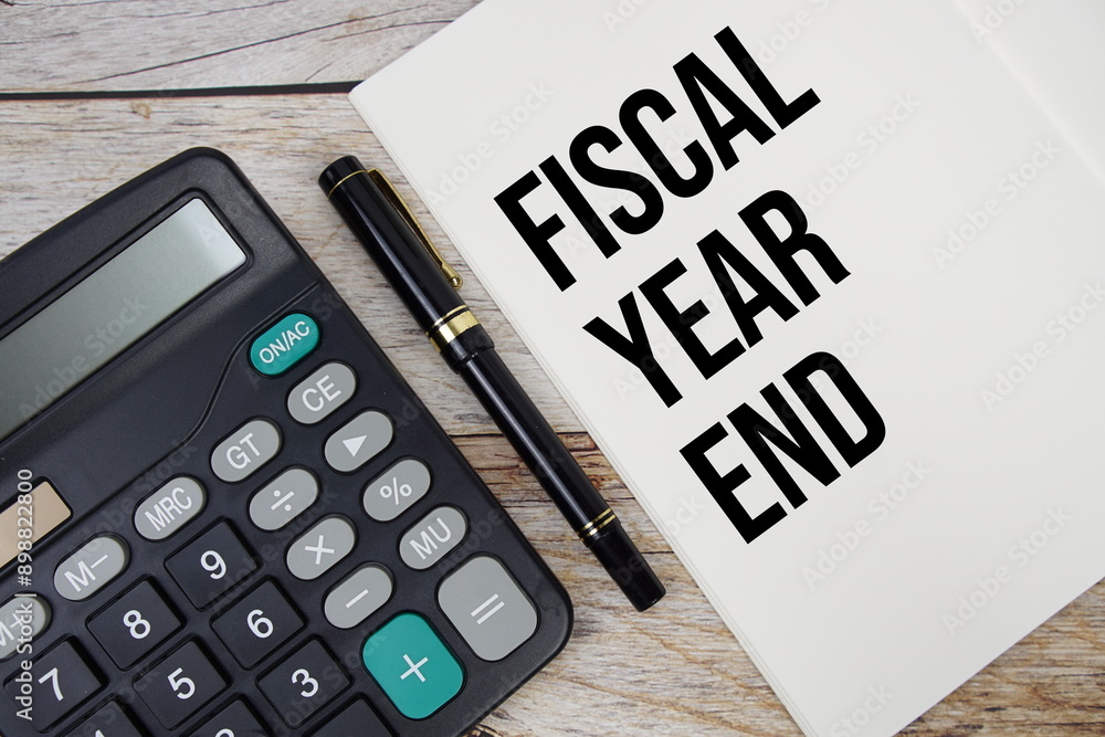 Aufkleber fiscal year end text message written on note page with calculator top view on wooden background