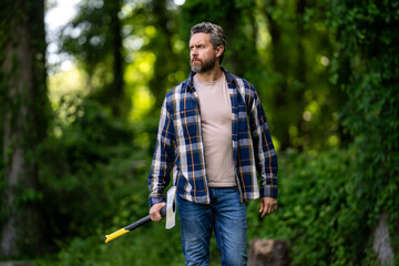 Fototapeta premium Bearded lumberjack. Lumberjack brutal bearded man in checkered shirt and ax in forest. Serious lumberjack holding axe and looking away outdoors. Lumberjack worker.