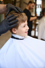 Attractive little boy sincerely laughing sitting in barber shop