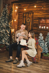 Obraz premium The atmosphere of the Christmas holidays. A happy family with a small child celebrates the New Year together near the Christmas tree in a cozy house. Christmas in the family circle.