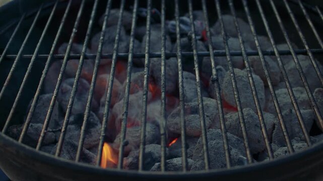 Extreme close-up shot of a brazier with grilling plate on and burning charcoal underneath. Embers and flame in a brazier with grilling plate, ready to roast barbecue.