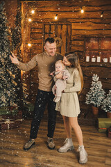 Obraz premium A young mother and father are standing with a small child near a Christmas tree. New Year's family holiday.
