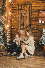 Obraz premium A family with a child on the background of a Christmas tree. A young man and a woman with a child in their hands in a New Year's house. Celebrating the new year in a family circle.