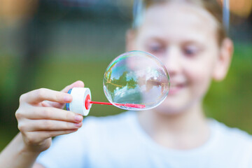 A little girl blows a huge soap bubble in the park in the summer. Blurred portrait with bokeh. 
