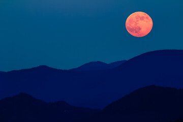 Red full moon over silhouette of mountains.