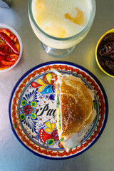 Close-up view from above of a traditional cemita in Puebla with a colorful Talavera plate in a metal container surrounded by different ingredients.