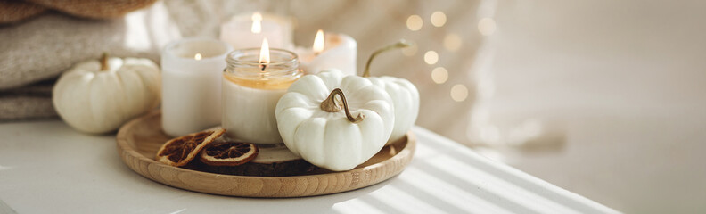 Autumn home decor with white pumpkins and burning aroma candles with sweet spicy pumpkin pie scent. Cozy fall composition, relaxation, aromatherapy. Apartment design, living room or bedroom banner