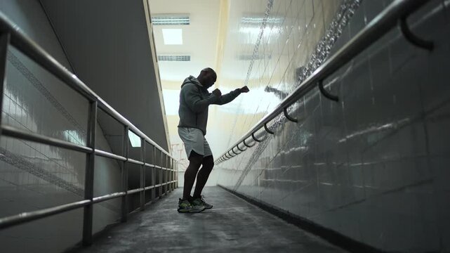 4K African man in sportswear do combat boxing exercise with punching the air in street crossing tunnel at night. Healthy guy athlete enjoy outdoor active lifestyle sport training workout in the city.