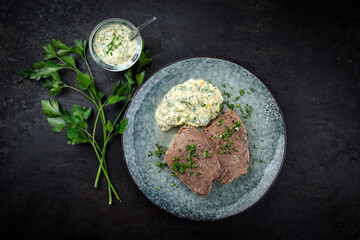 Cooked roast veal with sour cream sauce, eggs and chopped herbs served as top view on a Nordic design plate
