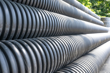 Stack of black HDPE storm sewer pipe (HDPE plastic N-12) on a project site awaiting installation.
