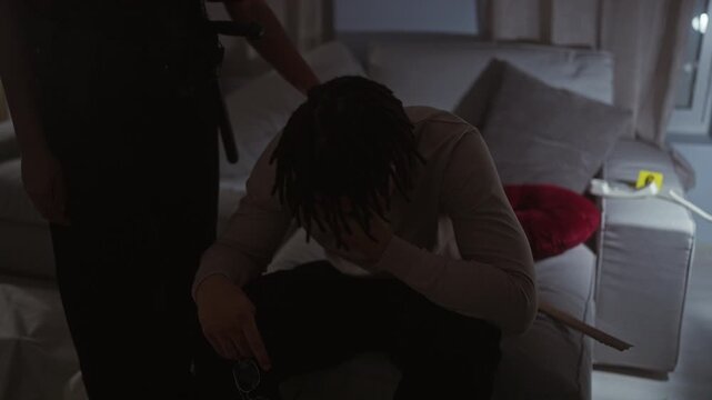Woman officer monitoring handcuffed man sitting dejectedly in a dimly lit interrogation room.
