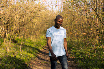 African american climate change volunteer leaving the clean forest area, feeling satisfied with his group work and perseverance. Happy smiling activist finishing litter cleanup.