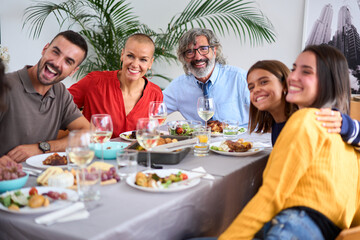 Portrait of cheerful Caucasian family posing with big smiles for a photo embraced indoor. Joyful people of diverse ages gathered sitting at table in a meal celebrating at home- Food and beverage