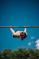 Athletic man practicing calisthenics on a pull-up bar in an urban park under clear blue sky....