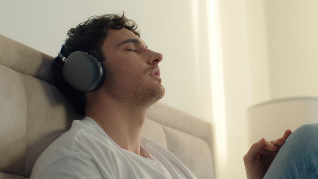 Caucasian man male guy listening music headphones closed eyes enjoyment relaxing sing song gadget technology playlist radio bedroom home satisfaction earphones audio device wireless connection sound