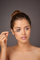 Fototapeta premium Mascara, makeup and face of woman on gray background for wellness, beauty and cosmetics. Cosmetology, salon aesthetic and girl with eyelash brush for application, lash extension and product in studio