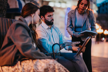 Young business professionals having an outdoor meeting discussing marketing strategies, brainstorming ideas, and analyzing reports for their small company's expansion.