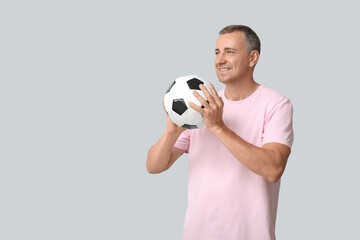 Handsome mature man playing with soccer ball on grey background