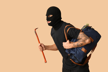 Male thief with crowbar and bag of money on beige background