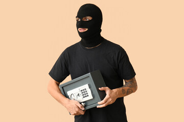 Male thief with stolen safe box on beige background