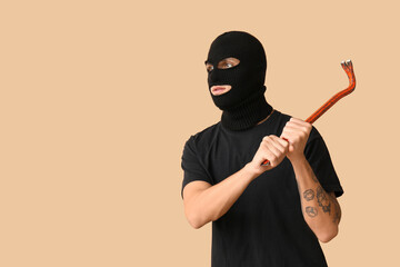 Male thief with crowbar on beige background
