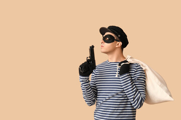 Male thief with gun and bag on beige background