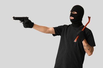 Male thief with crowbar and gun on grey background