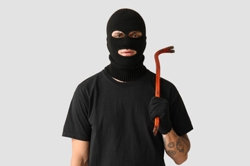 Male thief with crowbar on grey background