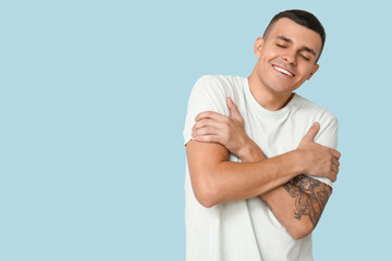 Handsome young man hugging himself on blue background
