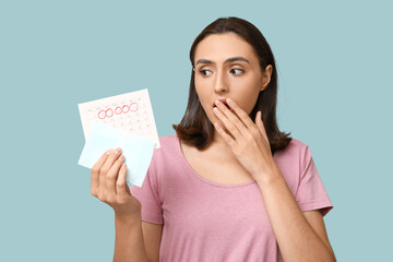 Beautiful shocked woman holding pad and calendar with marked days of menstruation on blue background