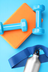 Two dumbbells, yoga block, fitness elastic band and thermo bottle on light blue background, flat lay