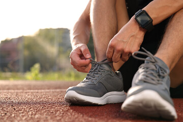 Fototapeta premium Man tying shoelace of grey sneaker at stadium, closeup. Space for text