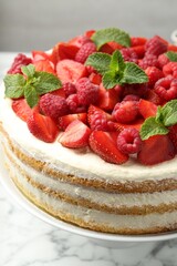 Tasty sponge cake with fresh berries and mint on white marble table, closeup