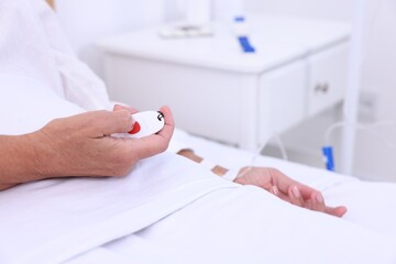 Senior woman pressing emergency call button on bed in hospital, closeup