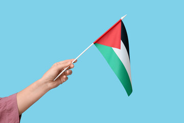 Female hand with flag of Palestine on blue background