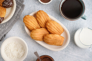 Plate with delicious madeleines, coconut flakes and cup of coffee on white grunge background