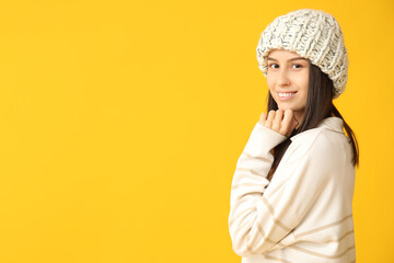 Beautiful young woman in stylish knitted hat on yellow background