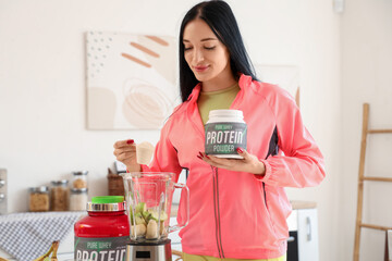 Sporty young woman with blender making protein shake in kitchen
