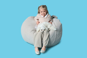 Cute little girl with Maltese dog sitting on beanbag chair against blue background