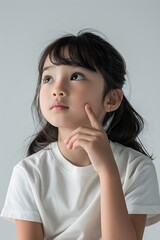 Little child thinking with hand on chin wearing t-shirt in studio on white background