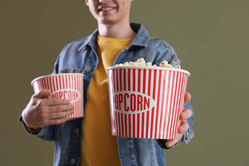 Young man holding buckets with popcorn on green background