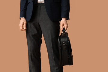 Young businessman with briefcase on brown background, closeup