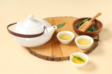 Wooden board with teapot, cups of tea, scoop and leaves on beige background